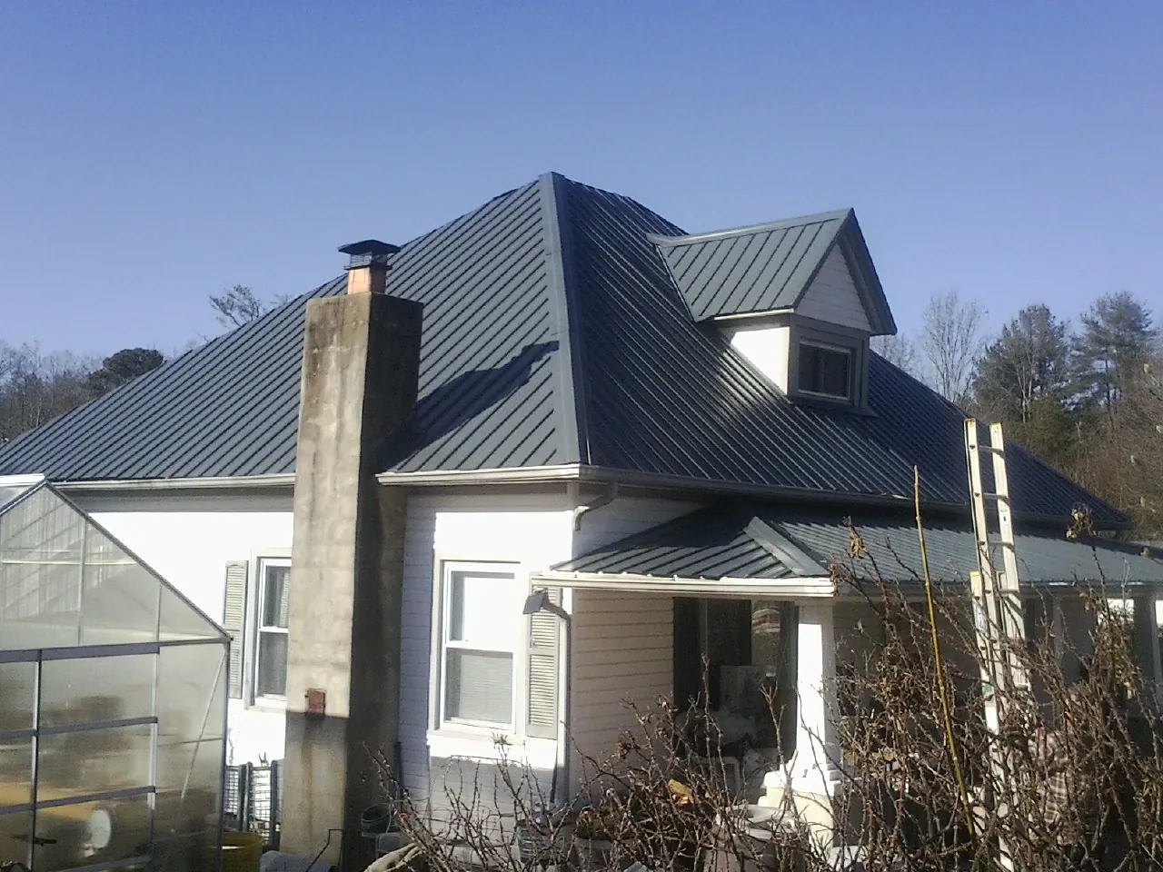 Dark blue standing seam metal roof on a white farmhouse with dormer — Slate & Tile Roof Repair by Roofing Brothers in Pineland