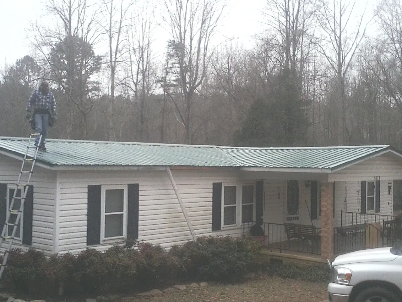 Worker on a ladder beside a new green metal roof on a ranch home in Pineland