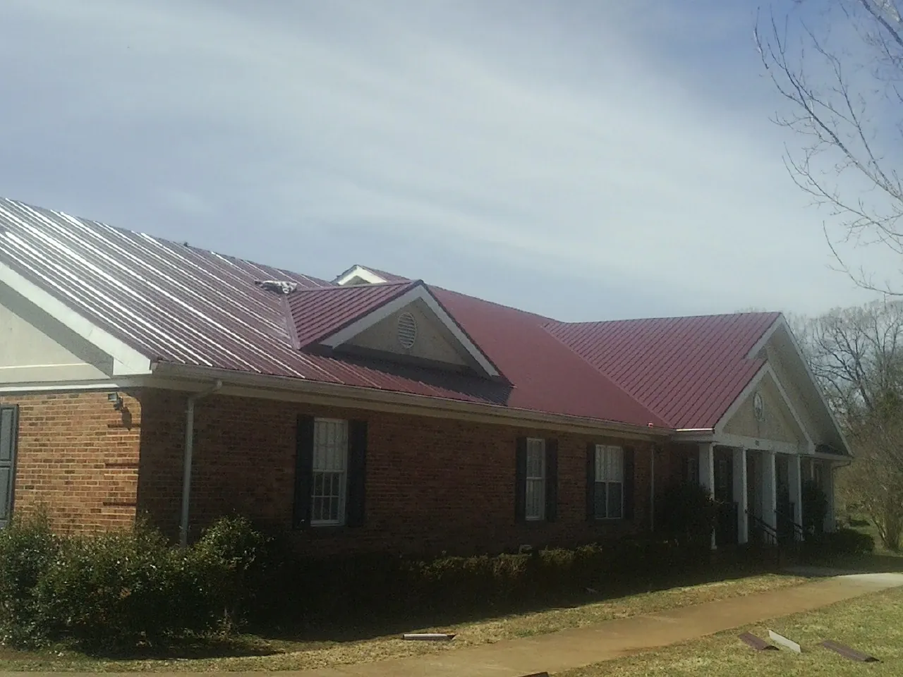 Red metal roof with gabled entries on a long brick building, from a Hail Damage Roof Repair job in Pineland