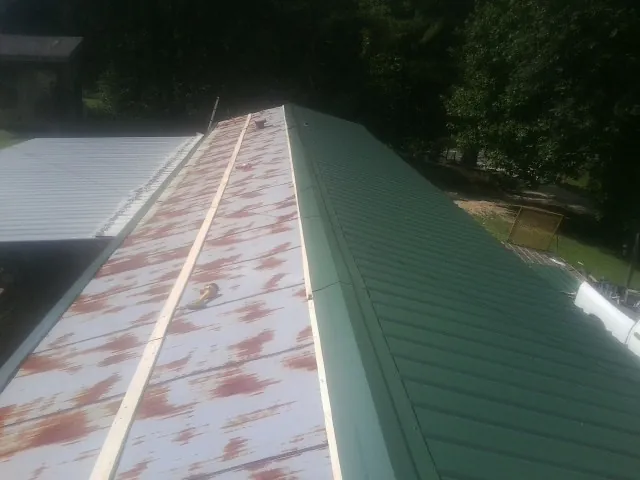 Old rusted panels beside newly installed green metal roofing — Wind Damage Roof Repair by Roofing Brothers in Pineland