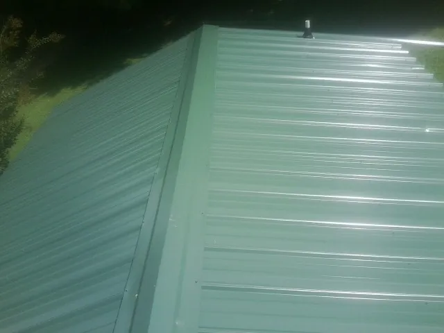 New green metal panels meeting at the ridge of a roof — Flat Roof Repair work by our crew in Pineland