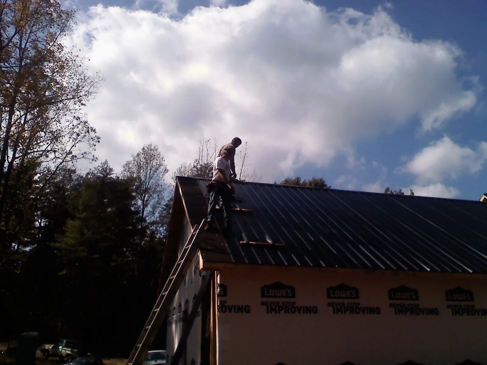 Roofer fastening dark metal panels high against a cloudy sky, from a Roof Inspection job in Pineland