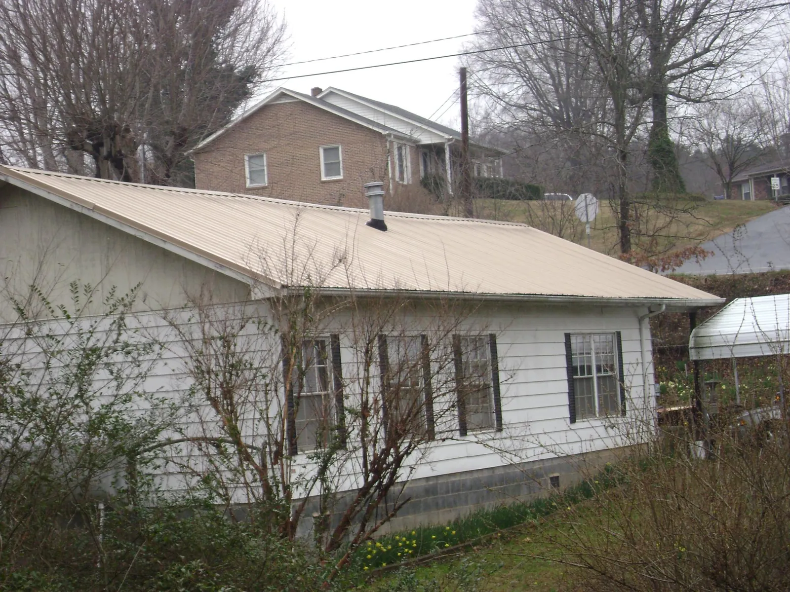 Tan metal roof on a white sided house set into a hillside — Commercial Roofing by Roofing Brothers in Pineland