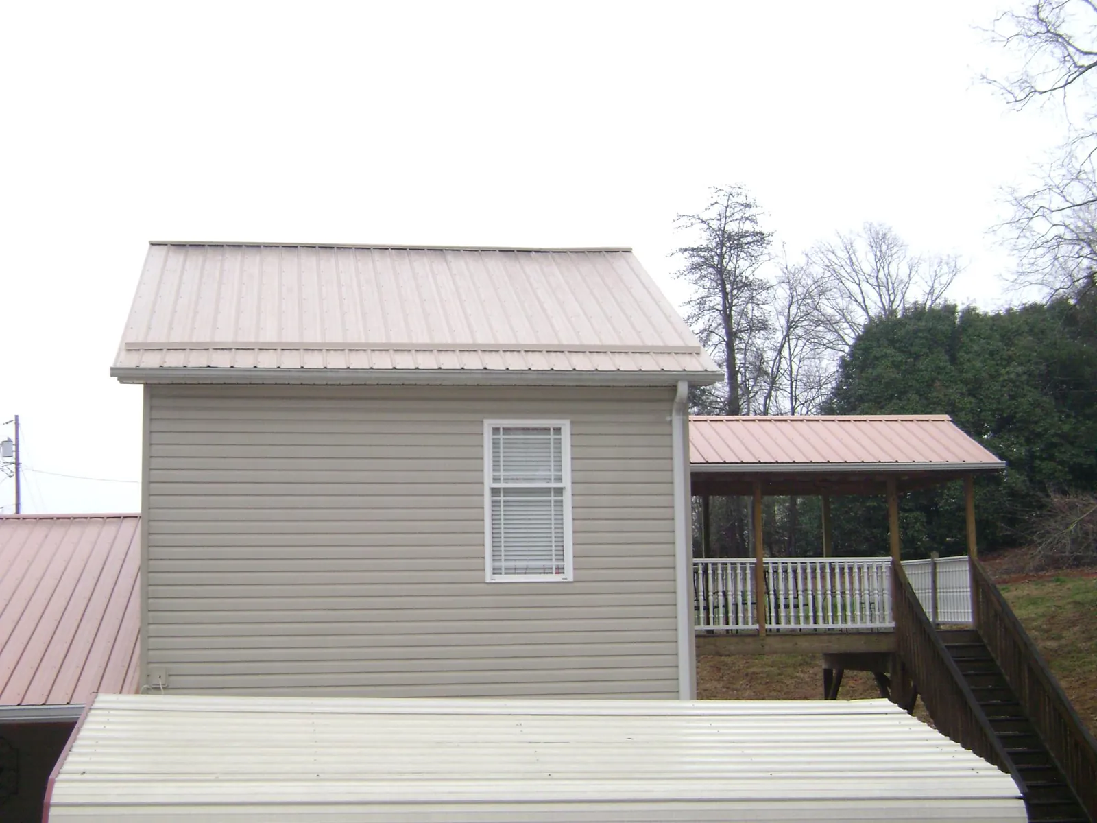 Tan metal roofs on a two story addition and attached porch, from a Roof Replacement job in Pineland